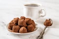 Chocolate truffle balls on a white plate. Heap of dark chocolate candies in cocoa powder, cup of coffee and spoon on a marble Royalty Free Stock Photo