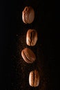 Chocolate and vanilla French or Italian macaroons falling on a black background, levitation. With cocoa powder and particles.