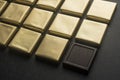 Chocolates in gold foil on black background.