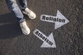 Choice between atheism and religion. Man standing near drawn marks on road, closeup. White arrows pointing in different directions