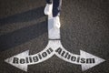 Choice between atheism and religion. Man walking towards drawn marks on road, closeup. Arrows with words pointing in opposite