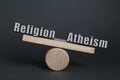 Choice between atheism and religion. Miniature wooden seesaw with words on dark grey background