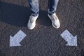 Choice of way. Man standing in front of drawn marks on road, closeup. White arrows pointing in different directions Royalty Free Stock Photo