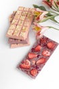 chocolate bar of handmade glutenfree chocolate with nuts and dry strawberry on white background with flowers