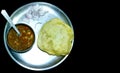 Chole Bhature or Chick pea curry and Fried Puri served in a plate and bowl over a black background