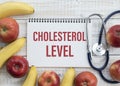 Cholesterol Level text on paper with stethoscope, delicious red apple, measurement tape and blue dumbbell on wooden