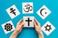 Choose religion concept. Hand with catholic cross near world religions symbols on blue background top view