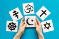 Choose religion concept. Hand with Islam crecent near world religions symbols on blue background top view