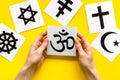 Choose religion concept. Hands with Buddhist Om sign near world religions symbols on yellow background top view