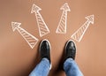 Choosing future profession. Man standing in front of drawn signs on brown background, top view. Arrows pointing in different Royalty Free Stock Photo