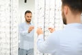 Choosing Glasses Concept. Portrait of handsome bearded guy picking new specs at optical shop, looking at mirror