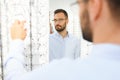 Choosing Glasses Concept. Portrait of handsome bearded guy picking new specs at optical shop, looking at mirror