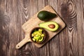 Chopped avocados in a bowl on cutting board on wooden background. Half avocado with pulp and seed, whole green fresh tropical Royalty Free Stock Photo