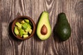 Chopped avocados in a bowl on wooden background. Half avocado with pulp and seed, whole green fresh tropical fruit on brown table Royalty Free Stock Photo