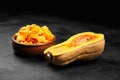 Chopped butternut squash, pumpkin half, fresh vegetable pieces in wooden bowl on black stone table Royalty Free Stock Photo