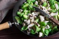 Chopped champignons and brussels sprouts in large skillet with knife, prepared for cooking