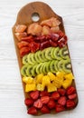 Chopped fresh fruits arranged on cutting board on white wooden surface, top view. Ingredients for fruit salad. From above, flat Royalty Free Stock Photo