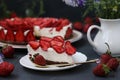Chopped homemade strawberry cheesecake, decorated with fresh strawberries, on a plate on a dark background, close-up, horizontal