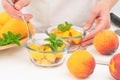 Chopped mangoes and peaches in a glass bowls with mint leaves close up on kitchen table, woman hands. Royalty Free Stock Photo