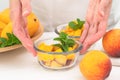 Chopped mangoes and peaches in a glass bowls with mint leaves close up on kitchen table, woman hands. Royalty Free Stock Photo