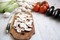 Chopped mushrooms on wooden chopping board and different vegetables over white wooden background, closeup. Side view. Royalty Free Stock Photo