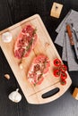 Chopped raw pork steaks with spices, tomatoes and thyme on a cutting kitchen board on a black wooden table. next to a napkin with Royalty Free Stock Photo