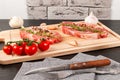 Chopped raw pork steaks with spices, tomatoes and thyme on a cutting kitchen board on a black wooden table. next to a napkin with Royalty Free Stock Photo