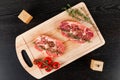 Chopped raw pork steaks with spices, tomatoes and thyme on a cutting kitchen board on a black wooden table. next to pepper shaker Royalty Free Stock Photo