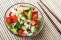 Chopped vegetables - cucumbers, tomatoes and onions in glass bowl and chopstick on bamboo mat. View from above. Copy space