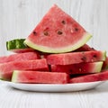 Chopped watermelon on a round white plate over white wooden background, close-up. Side view Royalty Free Stock Photo