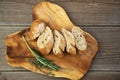 Chopped whole grain baguette with herbs on a wooden board, next to it are sprigs of green, fresh thyme and rosemary. View from