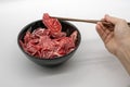 Chopstick holding fresh sliced beef hind shank from black cerami