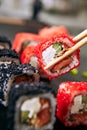 Chopstick holding maki sushi roll with rice, cream cheese, salmon, eel, cucumber, flying fish caviar. Nori maki rolls with raw tro Royalty Free Stock Photo