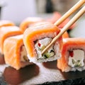 Chopstick holding Sushi Rolls Set with Salmon and Cream Cheese and Cuccumber on Black Slate Plate Close Up. Uramaki, Nori Maki or Royalty Free Stock Photo