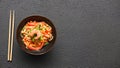 Chopsticks and a bowl with noodles wok vegetables and shrimp on a black table background with copy space Royalty Free Stock Photo