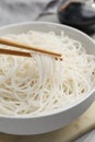 Chopsticks with cooked rice noodles over bowl on table, closeup Royalty Free Stock Photo