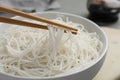 Chopsticks with cooked rice noodles over bowl on table, closeup Royalty Free Stock Photo