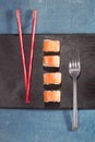 Chopsticks and fork with sushi on black plate