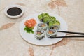 Chopsticks grabbing a homemade salmon sushi roll. White plate with salmon and shrimp japanese rolls, avocado and sesame seeds.
