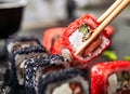 Chopsticks holding maki sushi roll with rice, cream cheese, salmon, eel, cucumber, flying fish caviar. Nori maki rolls with raw tr Royalty Free Stock Photo