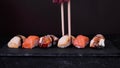 Chopsticks takes sushi with escolar from assorted sushi on a black plate on dark background. Minimal concept