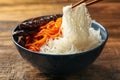 Chopsticks with tasty cooked rice noodles over bowl on wooden table, closeup Royalty Free Stock Photo