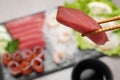 Chopsticks with tasty sashimi (piece of fresh raw tuna) against blurred background, closeup. Space for text Royalty Free Stock Photo