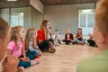 Choreography class. Young female dance teacher sitting on the floor with group of happy children in the dance studio Royalty Free Stock Photo