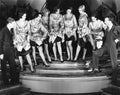 A chorus line of women showing off their legs to two men