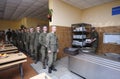 At a chow hall: soldiers stand in front of a serving bar and wait for kitchen worker preparing meal for distribution