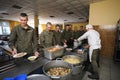 At a chow hall: soldiers stand in front of a serving bar and wait for kitchen worker preparing meal for distribution