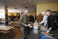 At a chow hall: soldiers stand in front of a serving bar and wait for kitchen worker preparing meal for distribution