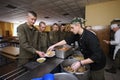 At a chow hall: soldiers standing in front of a serving counter for meal, kitchen worker distributing food