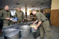 At a chow hall: soldiers standing in front of a serving counter for meal, kitchen worker distributing food